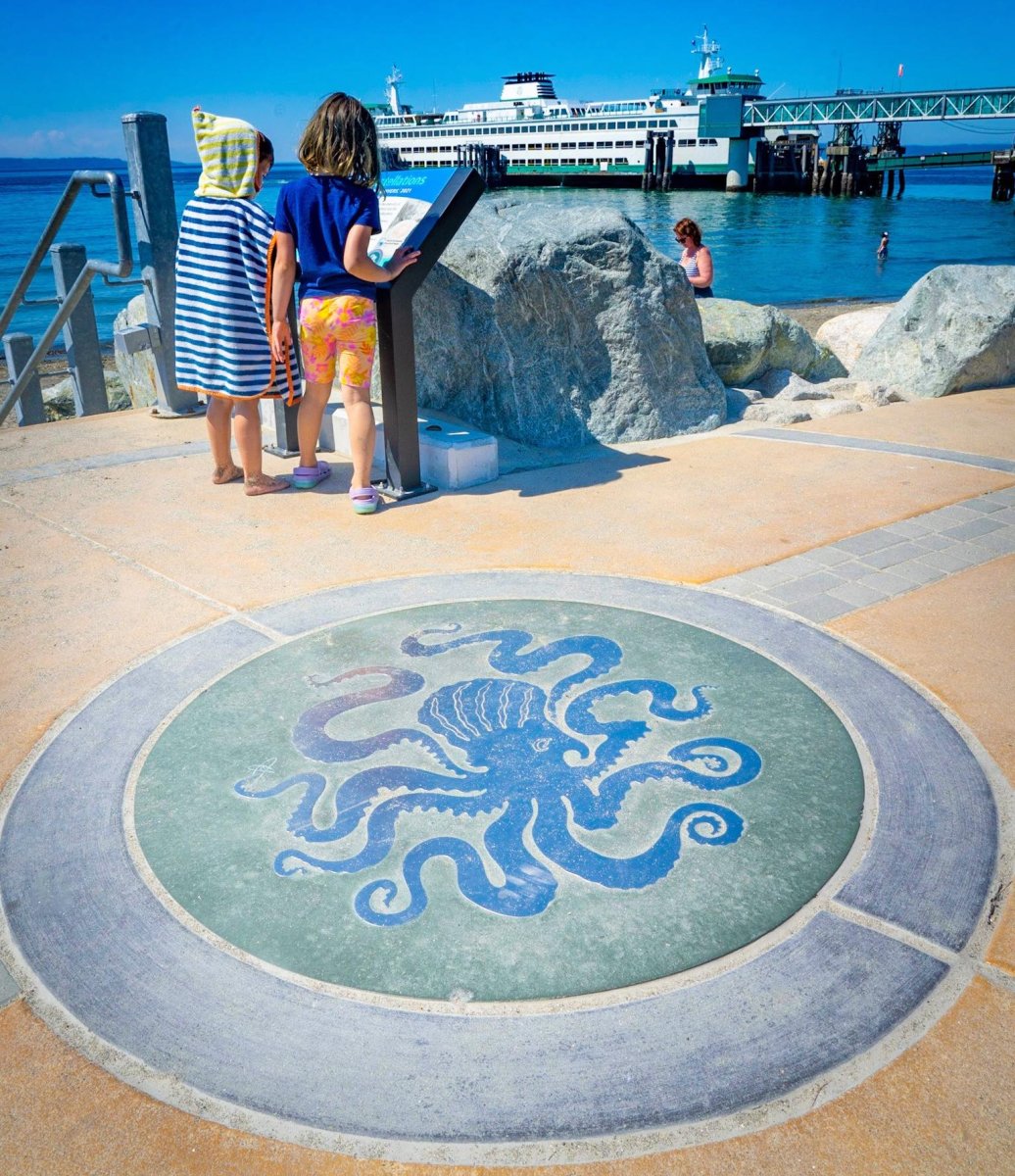 Two girls looking at a sign near octopus art inlaid in sidewalk on Edmonds waterfront